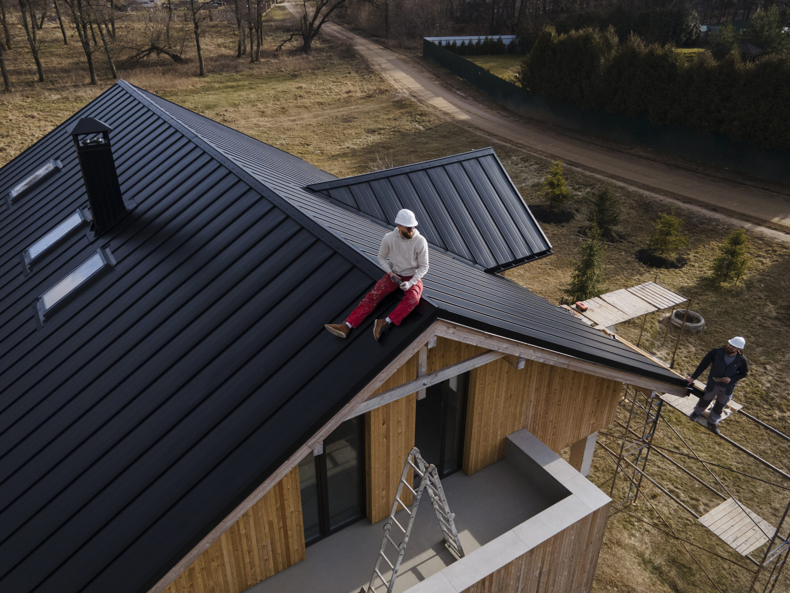 Roofer sits on metal roof on house while providing roofing services