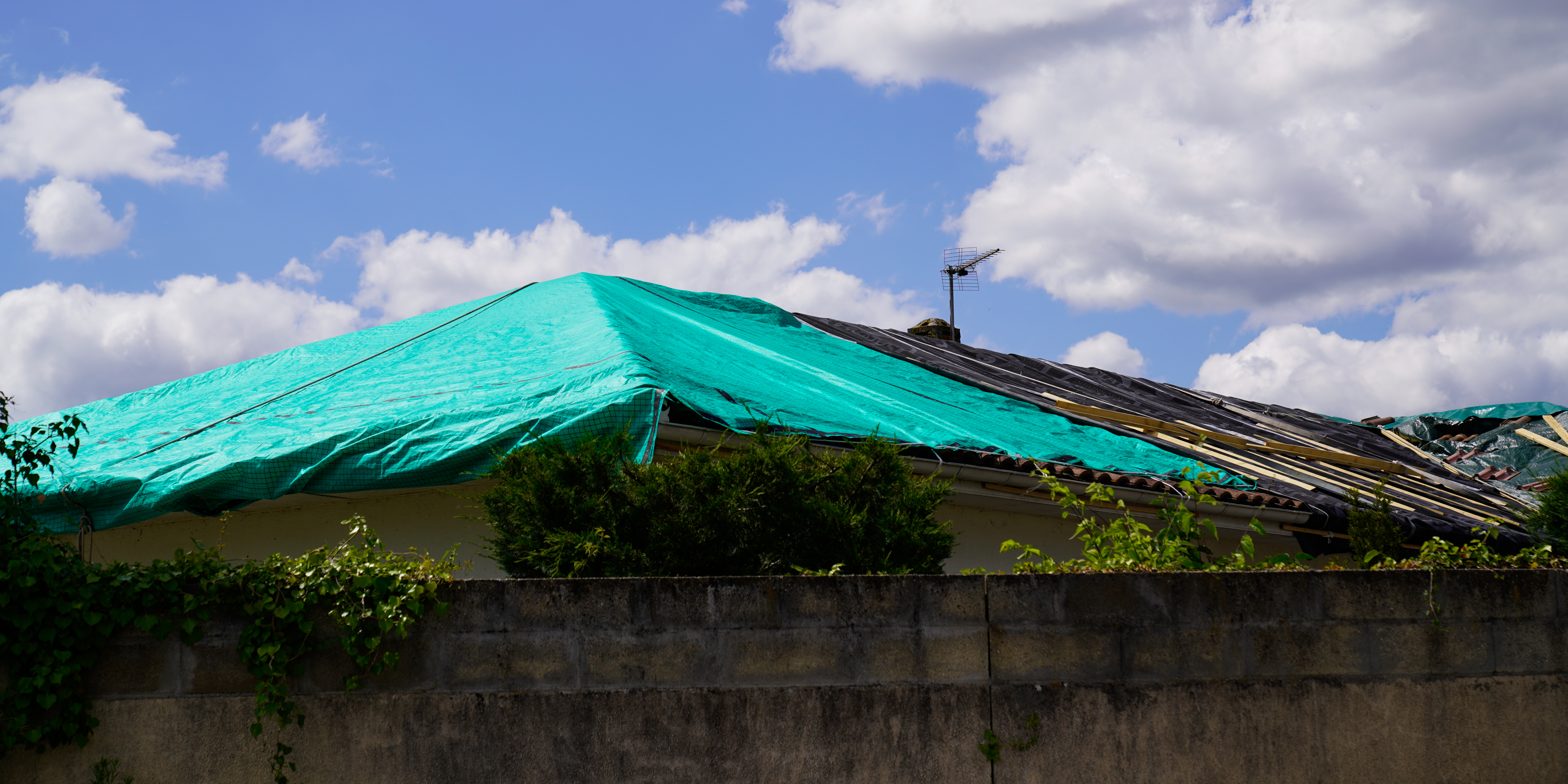 Green tarp covers storm-damaged roof waiting for roof repai