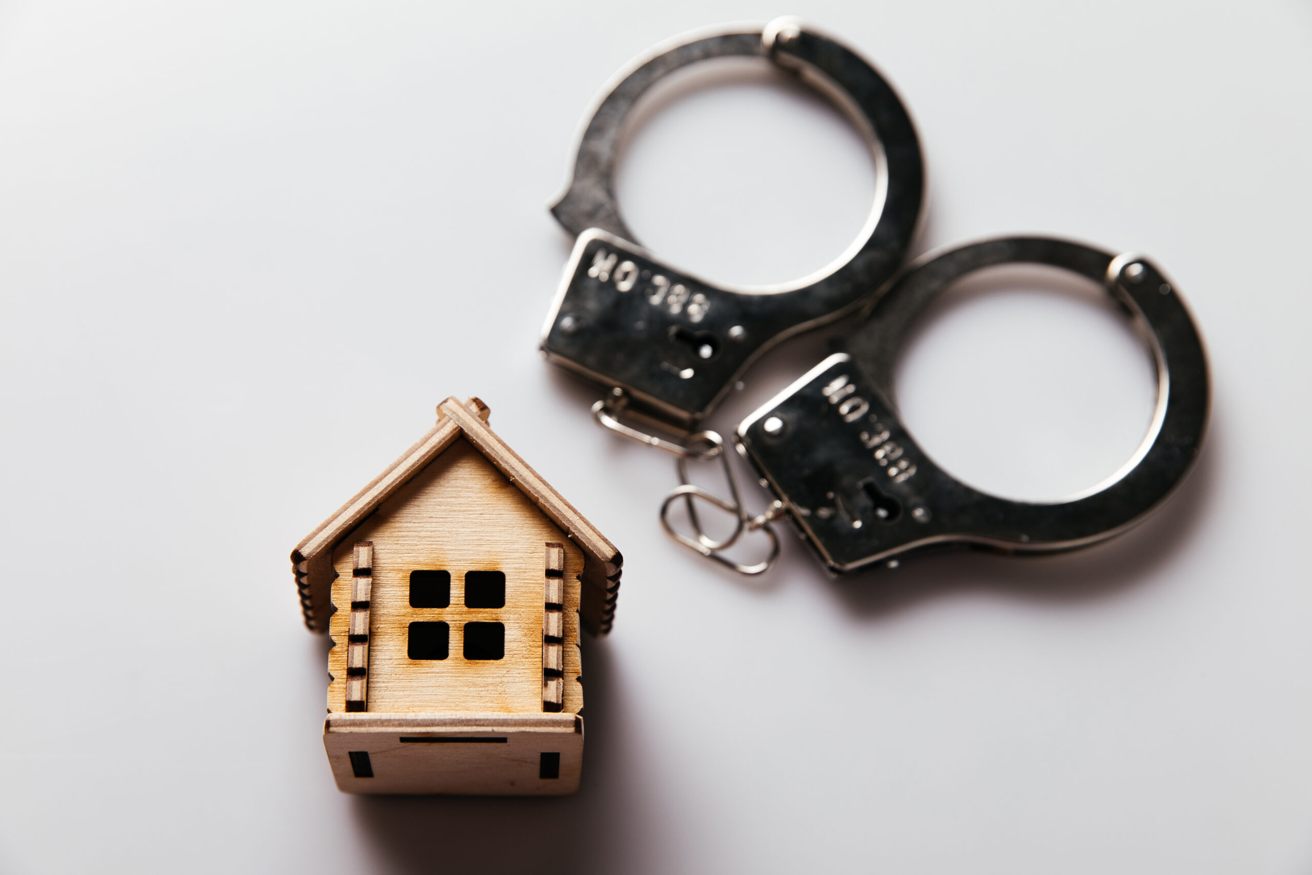 Mini wooden house beside handcuffs symbolizing roofing fraud and legal consequences
